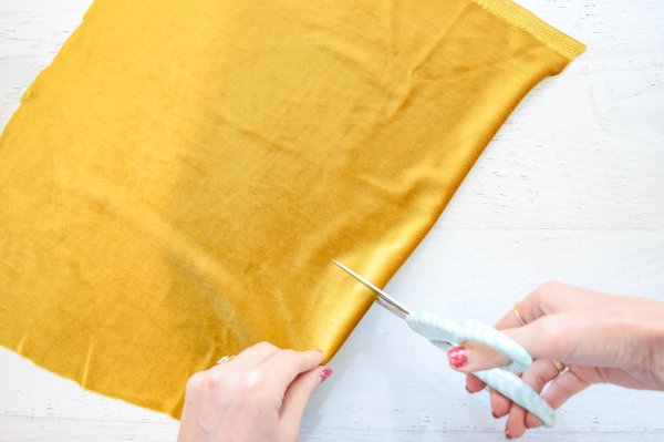 Abbi uses a scissors to cut the yellow-gold velvet fabric, which will be used to cover a paper mache pumpkin.