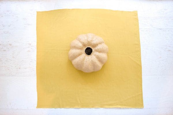 A paper mache pumpkin is placed in the middle of a large square of yellow velvet fabric.