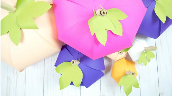 A pile of colorful paper pumpkins atop a wooden table.