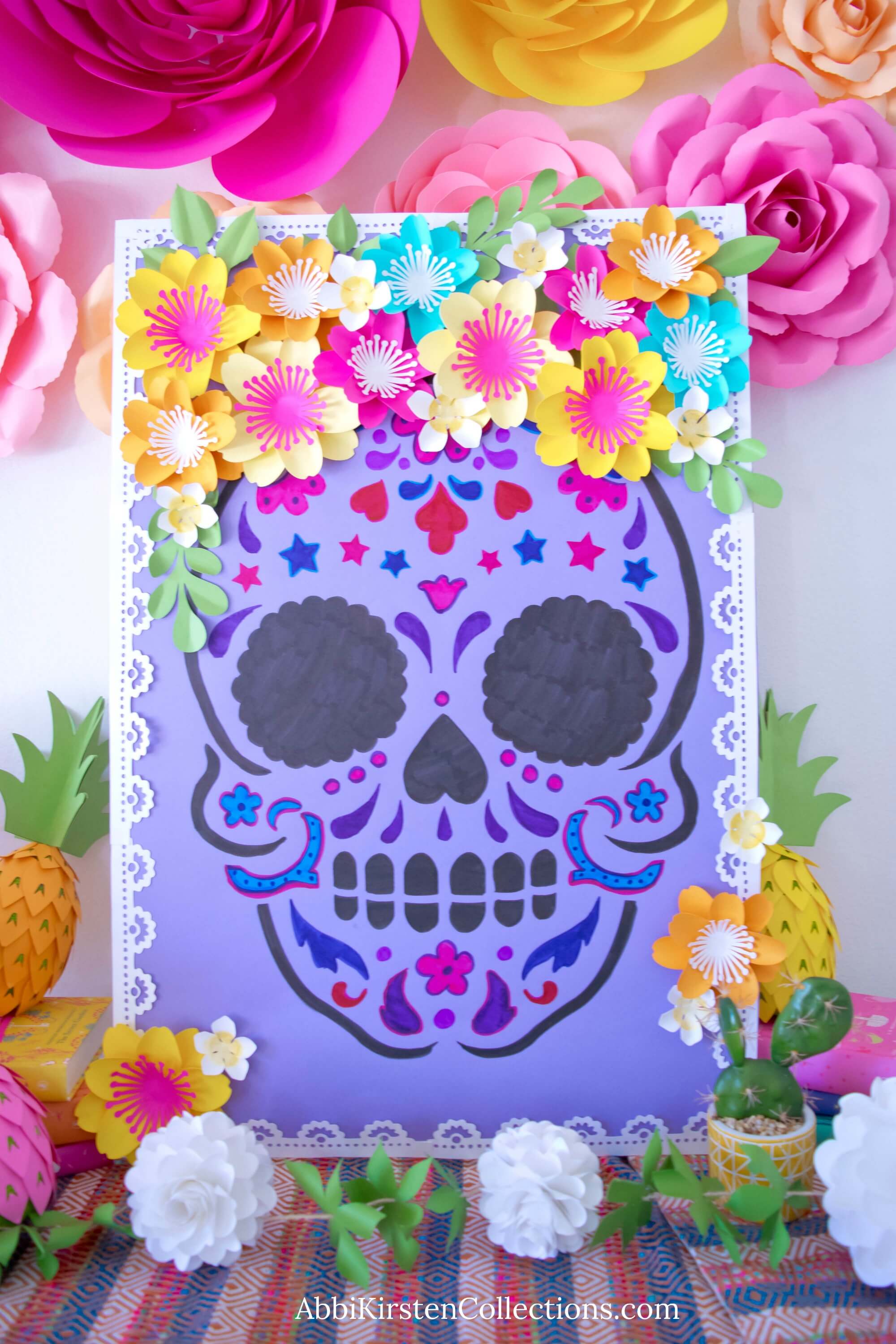 A colorful Day of the Dead poster with a sugar skull drawing. Paper flowers adorn the skull and the background.