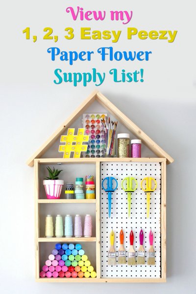 Text above a wooden open-framed house full of craft supplies reads "Paper flower supply list!"