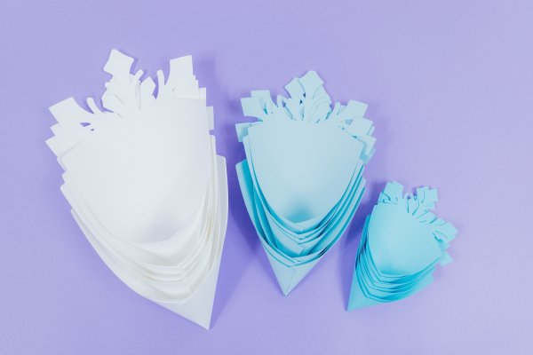 All of the various paper snowflake petals sit together, stacked, after being folded into a cone shape. There are three piles - larger light blue petals, sky blue medium sized petals, and robin's egg blue small petals.