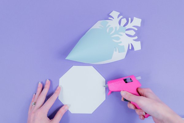 Abbi demonstrates how to add hot glue to the 8-sided paper snowflake base.