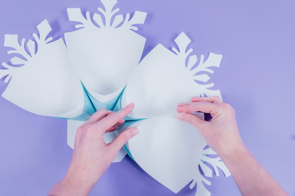 Abbi continues to glue paper snowflake petals to the base. In this image, four snowflake petals are glued to the base. Abbi holds two petals together.