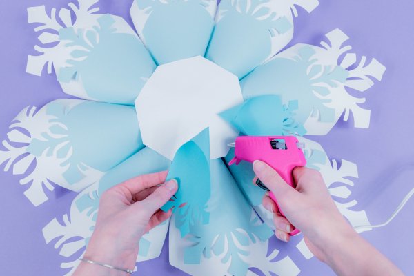 Abbi demonstrates how to glue the smallest snowflake petals to the front side of the snowflake base using a hot glue gun.