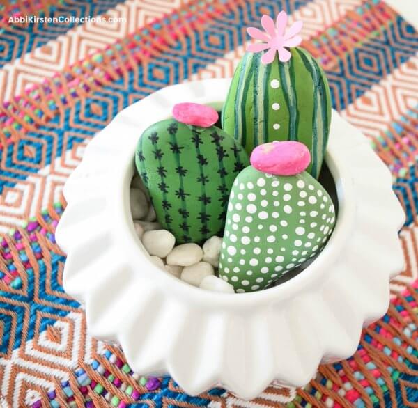 Three rocks painted as cacti arranged in a white planter. 