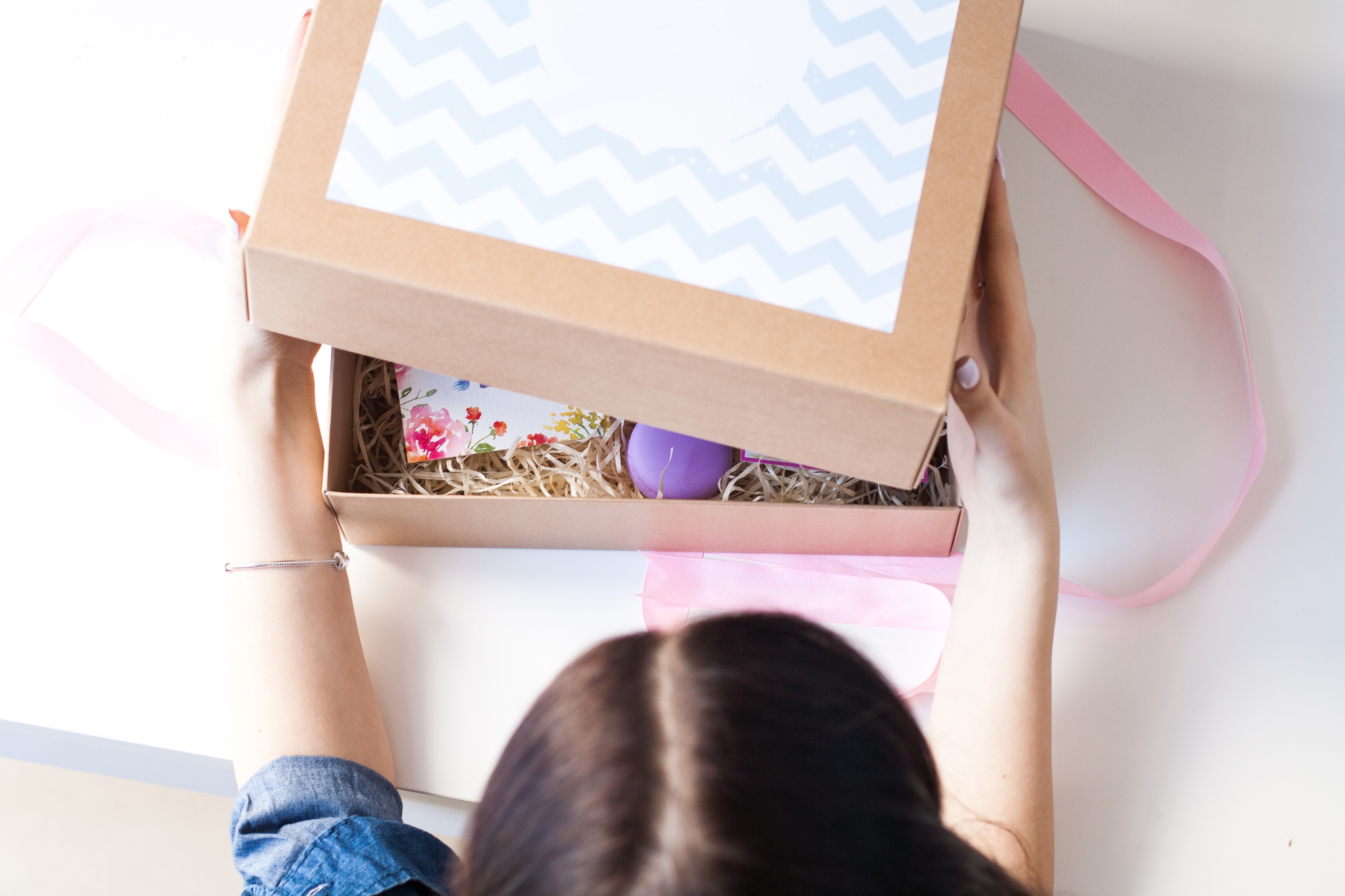 An overhead view of a dark-haired child opening a cardboard box with treasures inside. Starting a home craft business means understanding shipping materials.