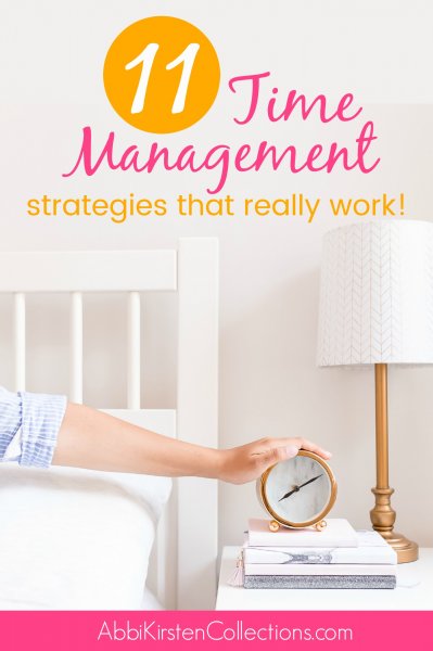 A graphic showing a woman's arm in pajamas reaches out from the bed with her hand on the top of a round analog clock set at 8:10. The alarm clock is on a nightstand on top of books, next to a lamp. The text on top says, "11 time management strategies that really work!" The bottom text reads, "Abbikirstencollections.com"