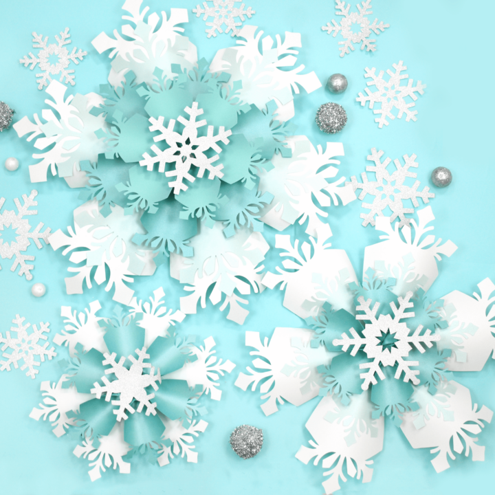 The image shows giant white and blue paper snowflakes made with Cricut. Get the templates on Abbi KIrsten Collections.
