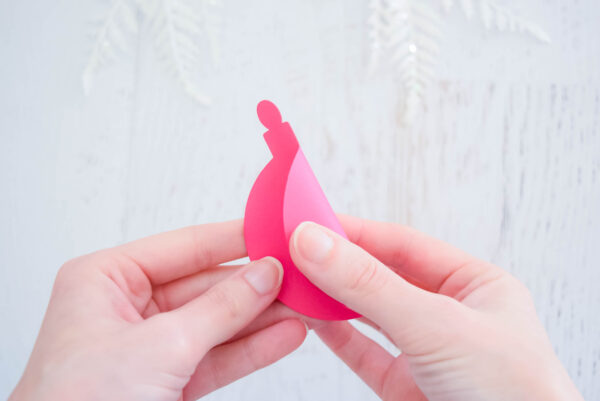 Abbi Kirsten's hand fold a pink paper ornament cutout in half. You can make 3D paper ornaments with Abbi's templates!