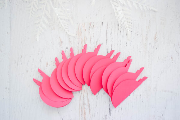 A bunch of paper ornaments folded in half on a wooden table. Snowflake decorations peek in from the top. You can use a Cricut or scissors to make these 3D Christmas paper ornaments. 