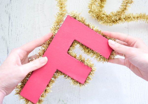 Abbi Kirsten adhered gold tinsel around every edge of a red letter "F" so that the letter is completely trimmed and ready to hang. 