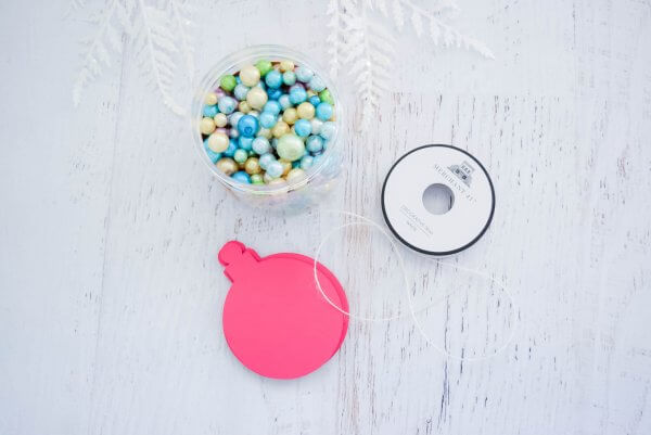 An unopened paper ornament, thread, and a jar of blue beads sit on a white wooden table-top. You can make your own 3D ornaments with this tutorial. 