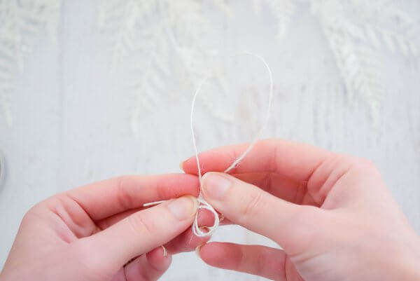 Over a white wooden distressed table, Abbi Kirsten forms a loop with white string. 