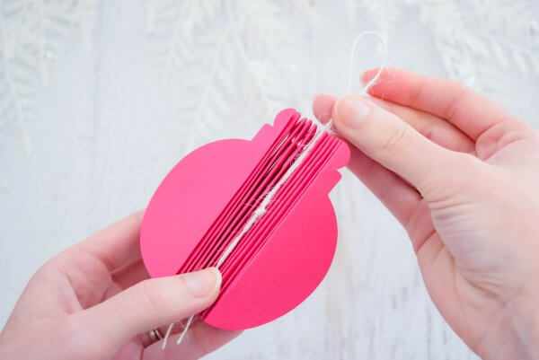 Abbi Kirsten's left hand holds a 3D paper ornament while pressing a piece of string into the center. Her right hand hold the string's loop above the ornament. 