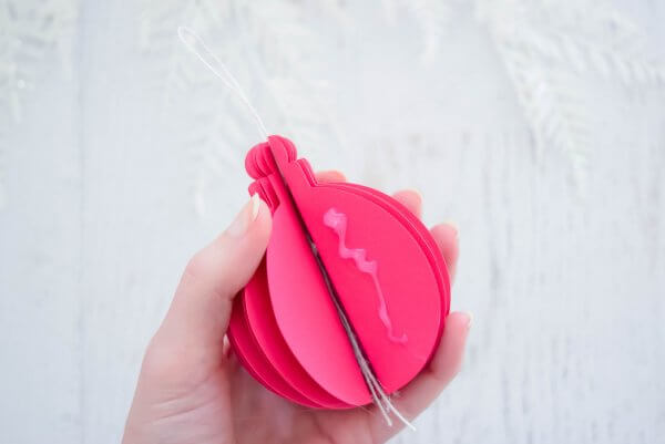 Abbi Kirsten holds a near completed 3D pink paper ornament. A squiggle of glue has been placed on one side of the ornament. 