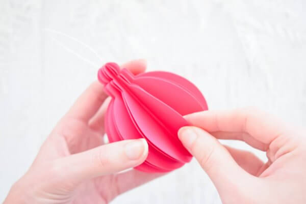 Abbi Kirsten uses her hands to fan out the layers of pink paper ornament for decorations or Christmas trees. 