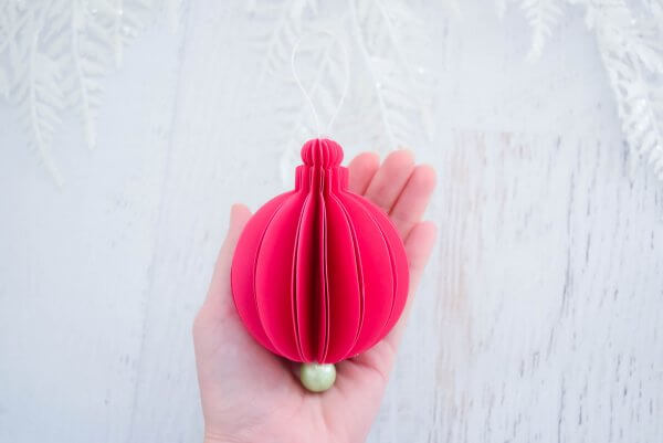 A finished 3D pink paper ornaments with a pearl base sits in the palm of Abbi Kirsten's hand. This is just one of nine templates for Christmas ornaments available on Abbi's site. 