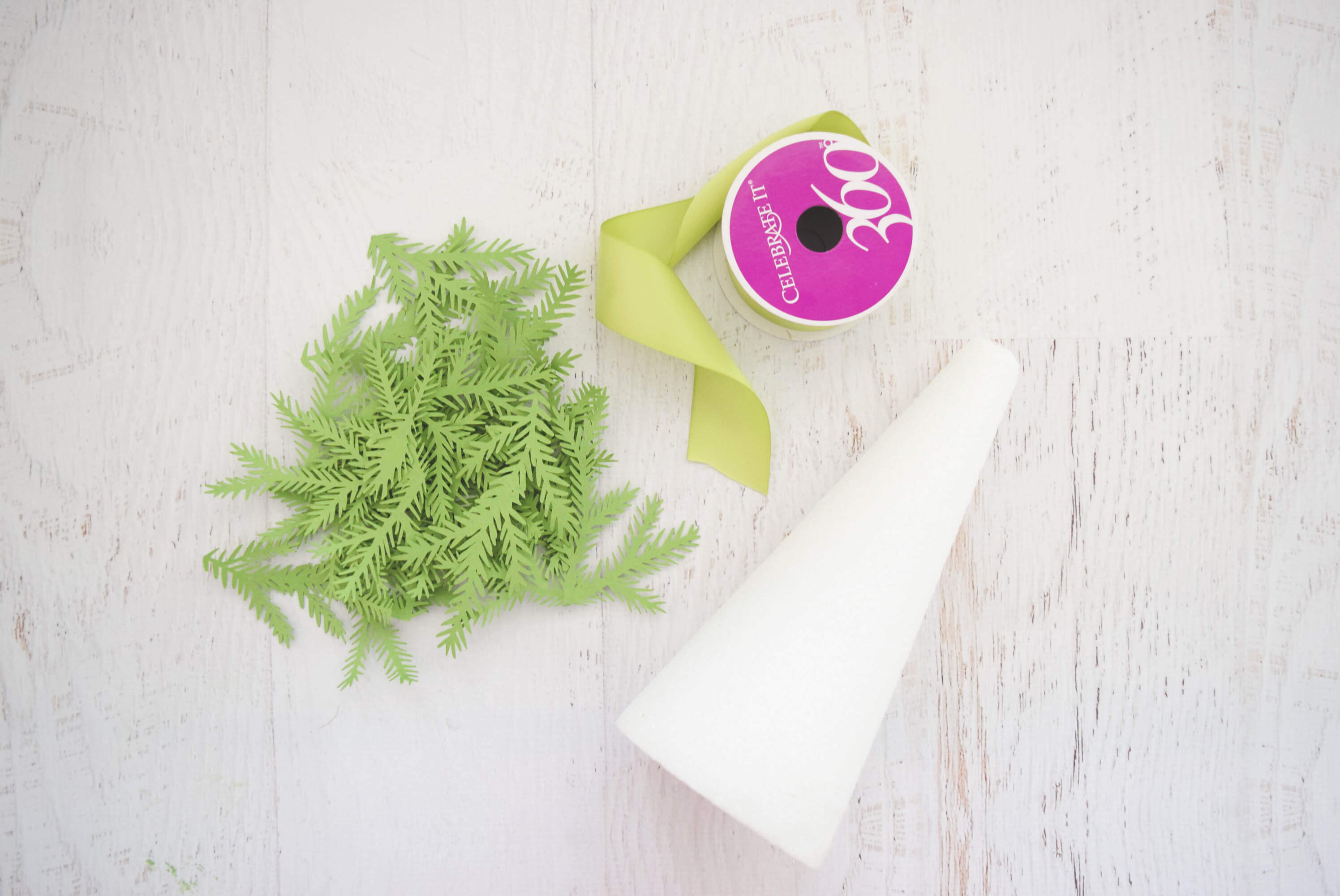 Supplies you need to make paper Christmas trees: paper leaves cut from green card stock, green ribbon, and a foam tree base.