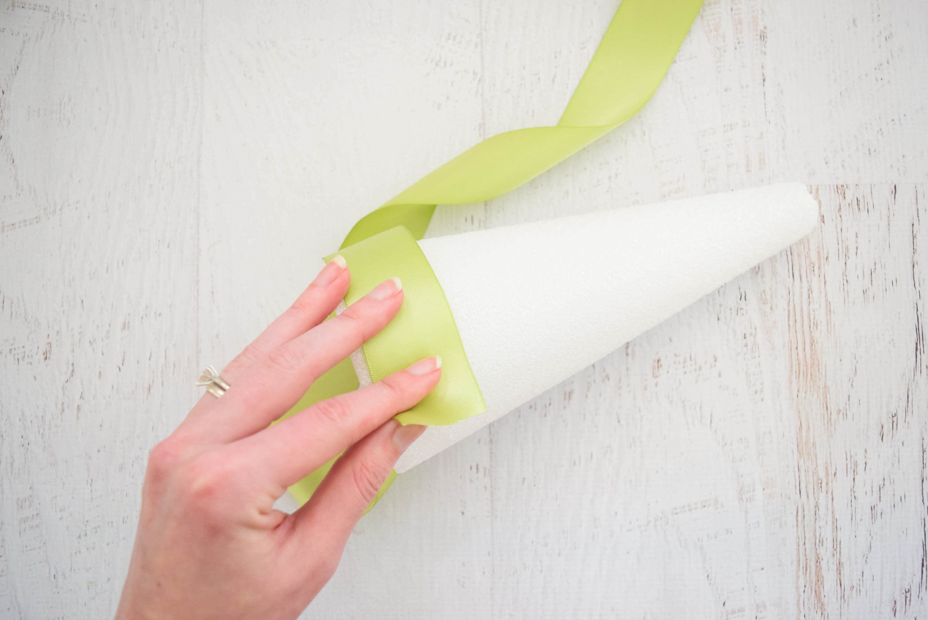 A woman's hand wraps green ribbon around a white foam cone base.