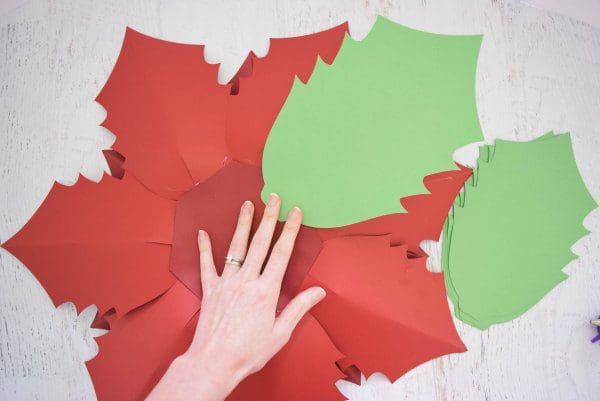 Abbi demonstrates how to add the green leaves to the bottom of the poinsettia flower base.