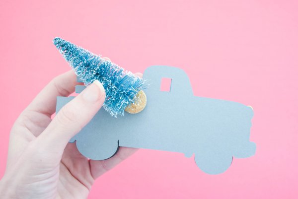 Abbi holds the bent bottle brush tree as the glue adheres to the back of the vintage Christmas truck ornament made from paper. 