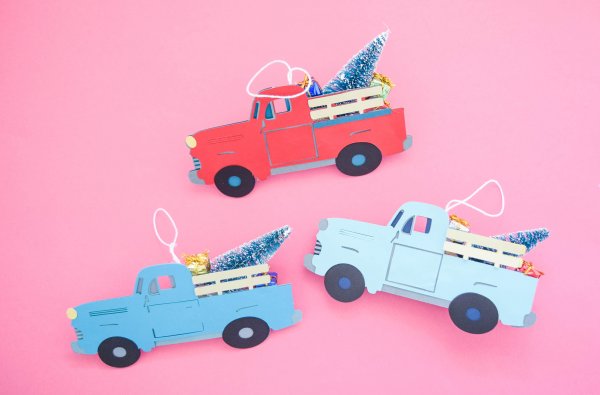 Three finished vintage Christmas truck ornaments, one red and two blue, have hanging strings added to the top, and Christmas trees and wrapped presents in the truck bed. These cute holiday ornaments are made with a free SVG file. 