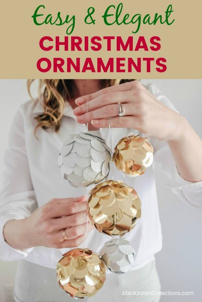 Abbi Kirsten, dressed in white, holds stringed gold and silver Christmas ornaments made of shiny paper and paper scales. The text reads "Easy and elegant Christmas Ornaments."