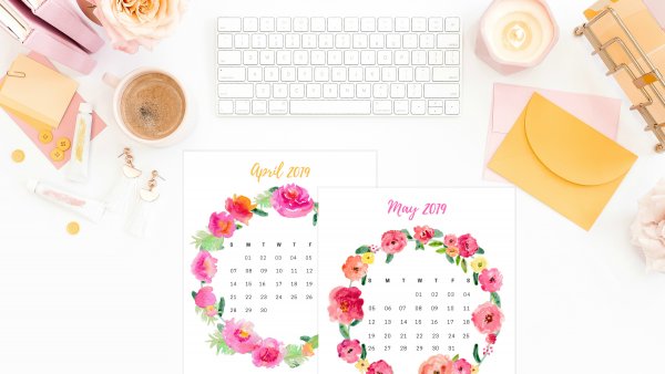 Calendar sheets with flowers around the days lay on a desk next to other office supplies. You can get your free 2019 printable calendar here. 