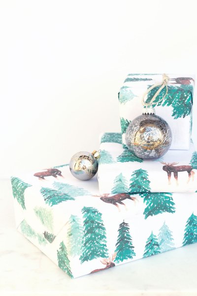 Moose and pine tree illustrations grace the white printable gift wrap. These two wrapped presents sit on a white background with silver Christmas baubles as decoration.