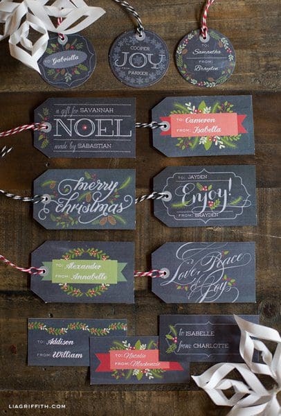These nine chalkboard gift tags on a dark wood table are printable and customizable. Each tag has a holiday phrase like "Merry Christmas" and "Noel."