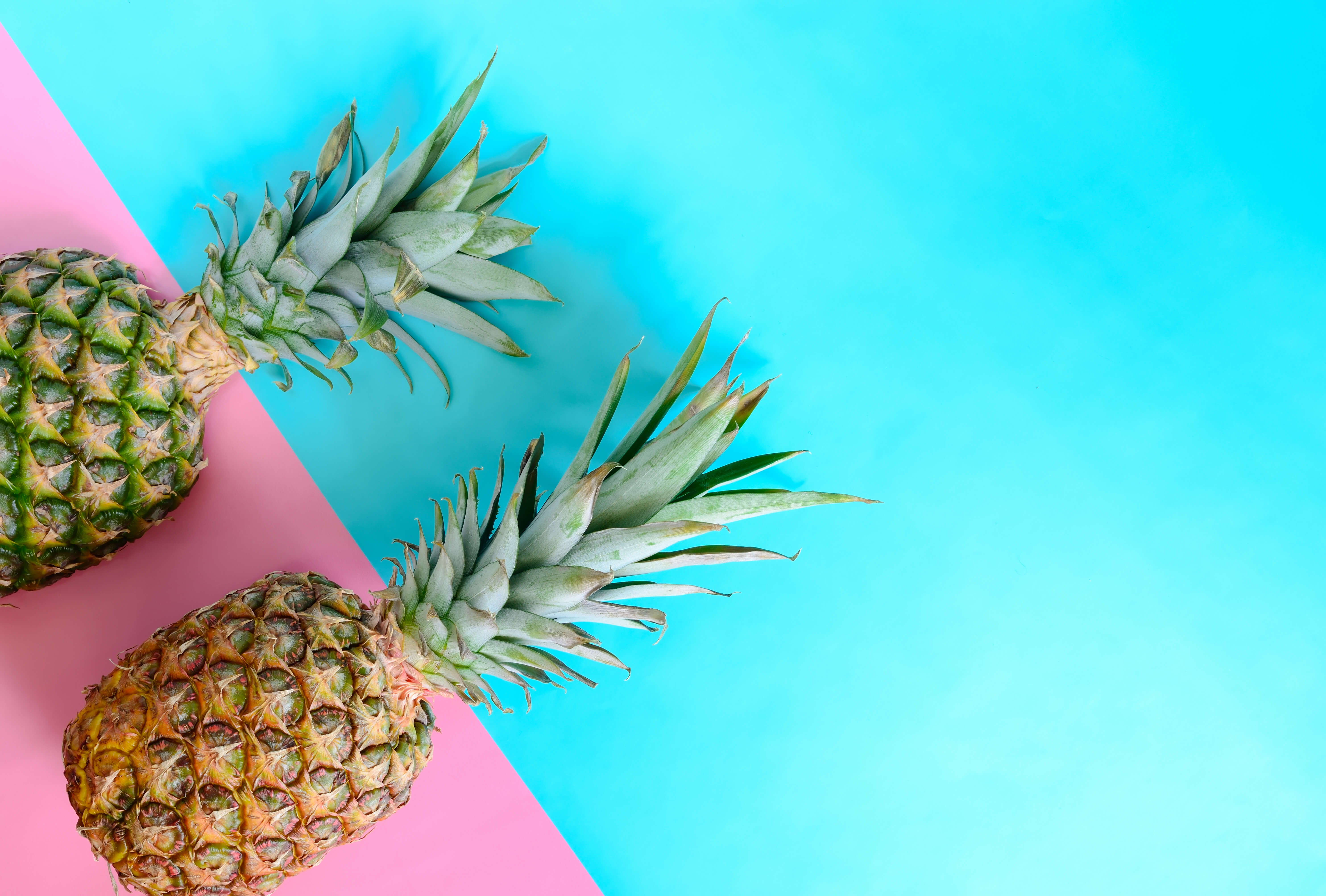 Two pineapples against a hot pink and turquoise blue background. 