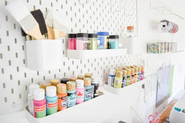 A pegboard wall allows for customized craft room organization. You can use shelves or bins to hold smaller supplies like paint and brushes on a wall organizer. 