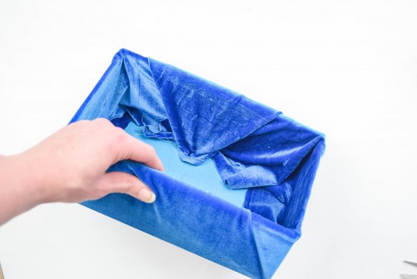 Abbi demonstrates how to pull the velvet fabric tight so it can be glued inside the box neatly. These step-by-step instructions make it easy to craft your own fabric storage box. 