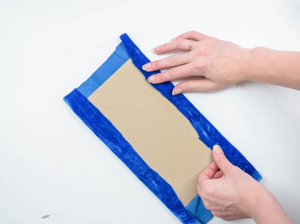 Abbi glues a cut piece of blue velvet to the chipboard so that it can be placed in the DIY fabric storage box. 