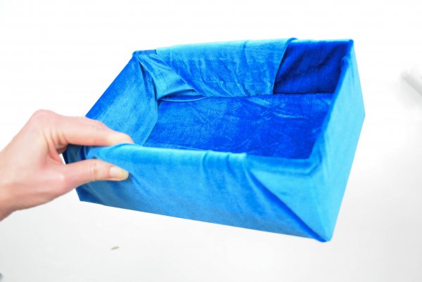 Abbi Kirsten's hand holds the finished luxury DIY fabric storage box wrapped in blue velvet. 