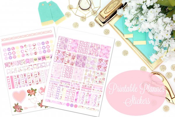 An overhead view of two sheets of pink February Planner stickers surrounded by teal and gold tags and office supplies. The pink circle has white text that says "printable planner stickers" in a script font. 