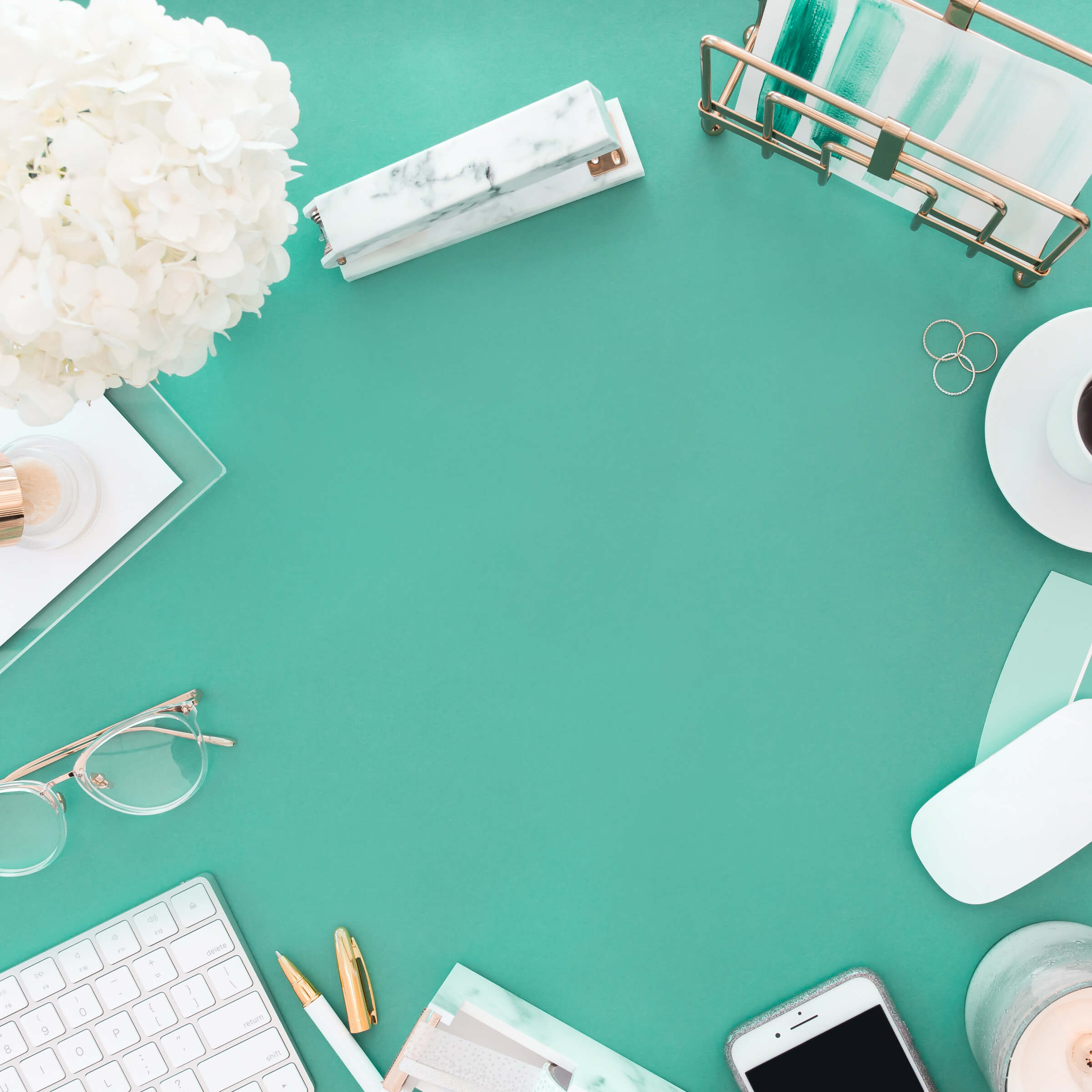 A bright seafoam green desk with cream and rose gold accessories placed around the outside of the image.  