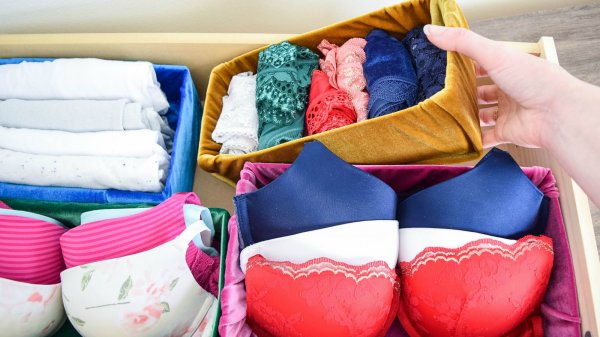 Abbi puts a mustard-colored velvet fabric-wrapped cardboard box into her undergarment drawer. There are other fabric covered storage boxes that are organizing parts of the drawer.