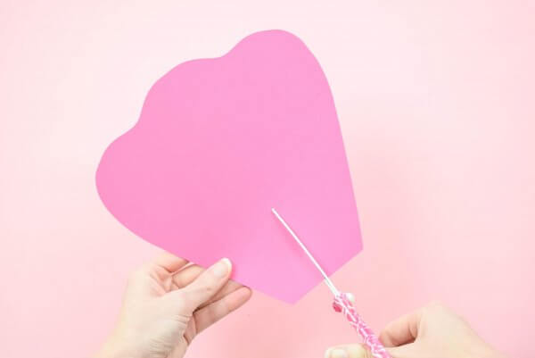 Abbi Kirsten holds an extra-large pink petal as she cuts a slit from the bottom to the middle of the paper flower. 