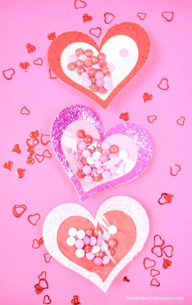 A pink paper backdrop holds three paper candy-filled hearts lined up down the center of the picture. Free SVG files are available!