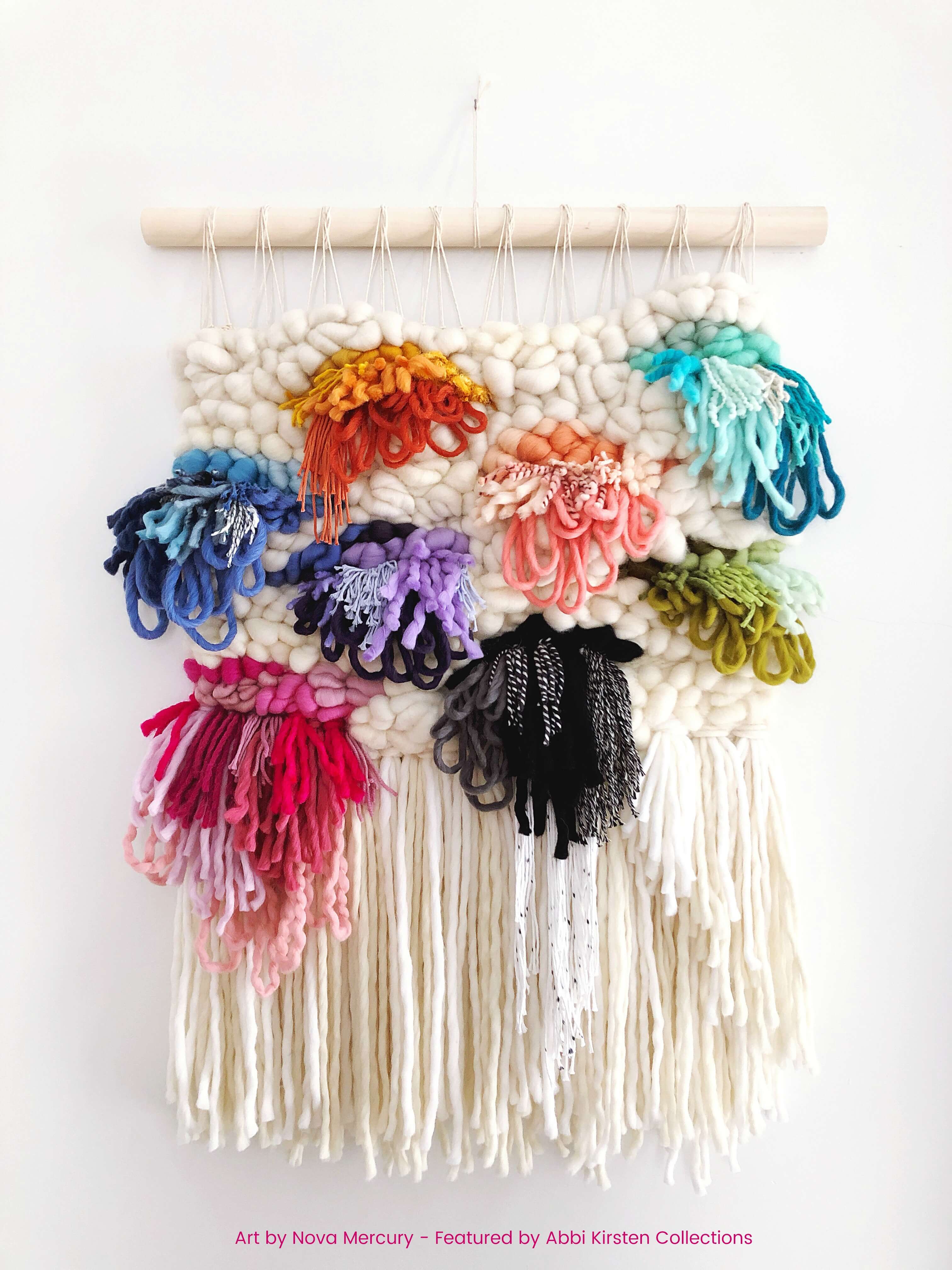 A large, colorful modern macrame wall hanging features pops of colorful threads  against the cream background. The macrame wall art hangs from a thick wooden dowel rod.