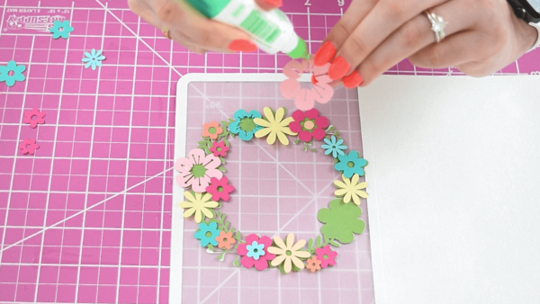 Pastel flower cutouts being glued onto a green wreath.