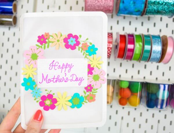 A DIY Floral Mother's Day Card being held by a hand against a wall of colorful ribbon and balls.