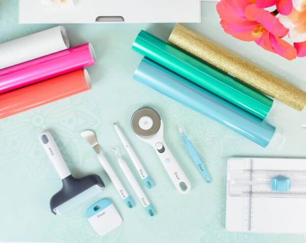 A tabletop full of crafting supplies like vinyl rolls and Cricut cutting tools. 