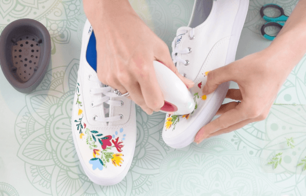 Abbi uses the Cricut Easypress Mini to apply vinyl floral appliques to a pair of white shoes.