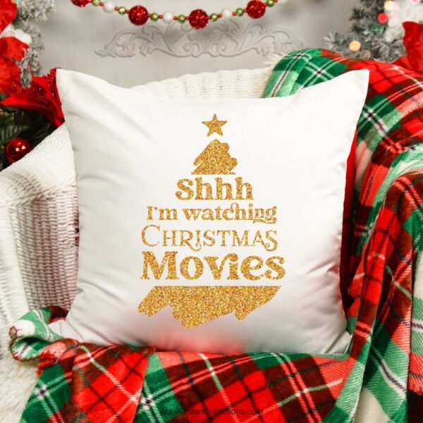 The images show a White Christmas pillow throw pillow on a red and green plaid blanket. The pillow has a gold vinyl graphic that says, "Shh I'm watching Christmas movies."