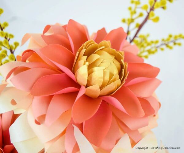 A closeup of a paper dahlia in autumn shades of pink, peach and orange, with a yellow center. 
