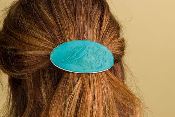 The back of a woman's head. She has some of her hair gathered in a leather barrette, which has been engraved with a Cricut cutting machine. 