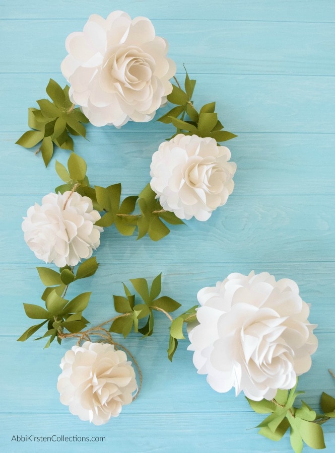 A DIY paper flower ball garland made with white paper pomander flowers connected with twine and green leaves.